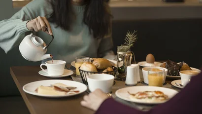Frau gießt Tee bei Frühstück mit Brötchen und Eiern