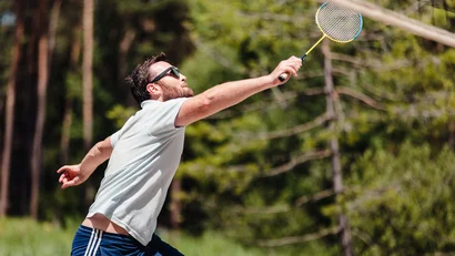 Mann spielt Badminton im Freien mit Waldhintergrund