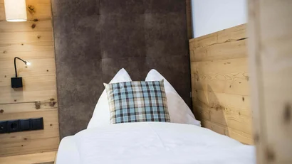 Einzelbett mit Kissen und weißen Bettlaken in Holzzimmer