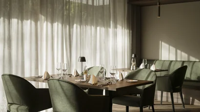 Elegantes Restaurant mit gedeckten Tischen und grün bezogenen Stühlen bei Tageslicht