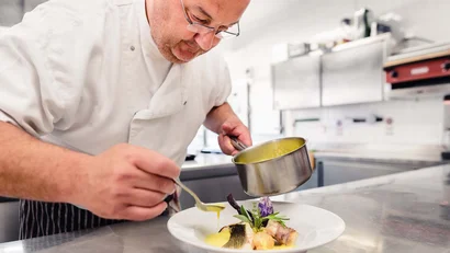 Koch gießt Sauce auf ein Gourmetgericht in einer professionellen Küche