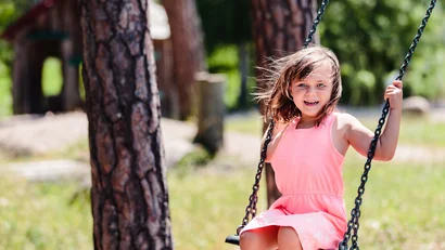 Mädchen in rosa Kleid auf Schaukel im sonnigen Park