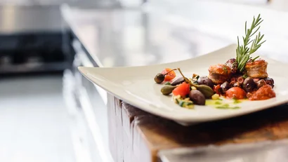 Gourmetgericht mit Oliven, Tomaten und Kräutern auf weißem Teller