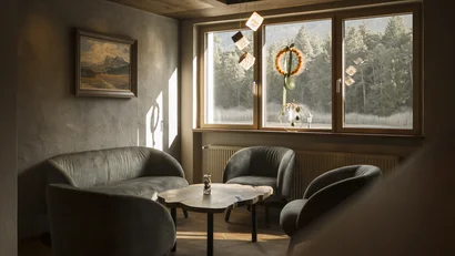 Gemütliche Sitzecke mit Sesseln und Sofa vor Fenstern mit Waldsicht