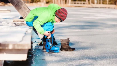 Kind zieht blaue Schlittschuhe auf gefrorenem See an