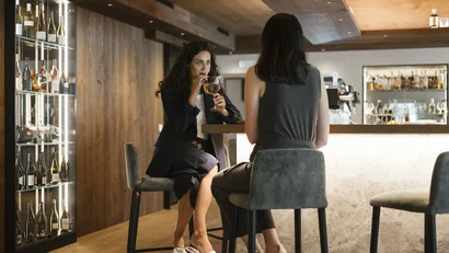 Two women sitting at a bar drinking in a modern bar setting