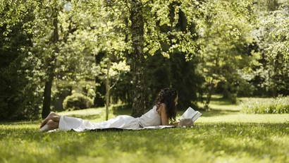 Woman lying on blanket reading a book in sunny park under trees