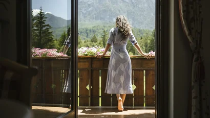 Woman on balcony with mountain view and flowers in sunlight