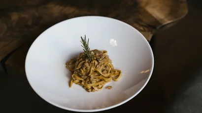 Tagliatelle mit cremiger Hackfleischsauce und Rosmarinzweig auf weißem Teller