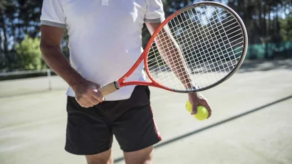Mann in Sportkleidung mit Tennisracket und Bällen auf Tennisplatz