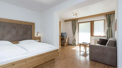 helle hotelzimmer mit bett, sofa, schreibtisch und tisch vor fenstern mit vorhängen