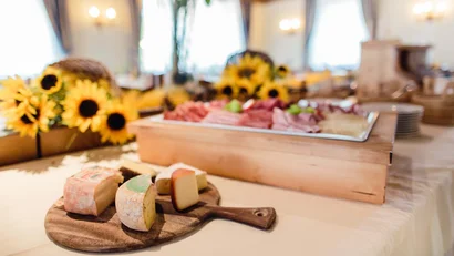 Holzbrett mit verschiedenen Käsesorten auf einem gedeckten Tisch mit Sonnenblumen
