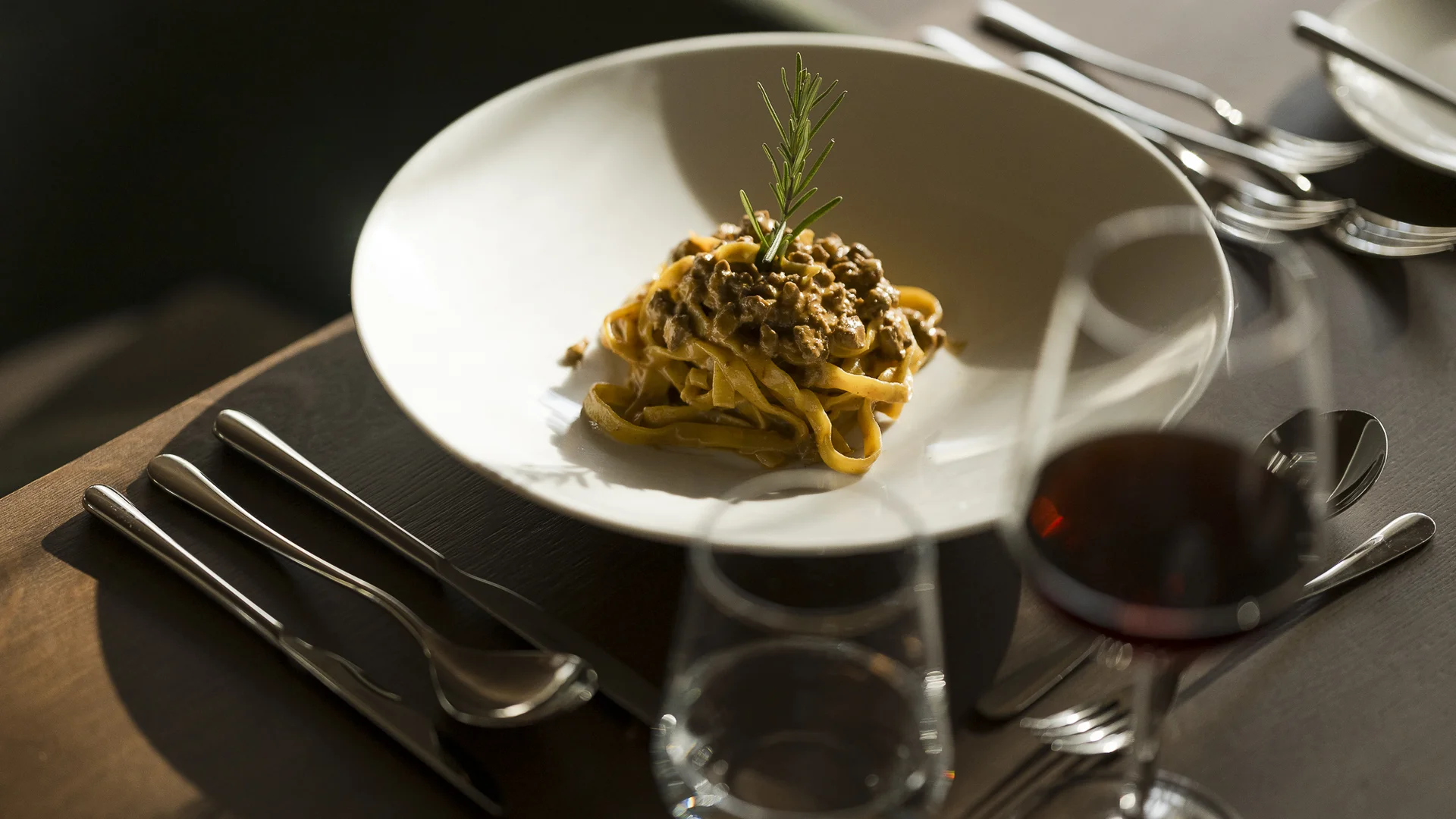 Pasta mit Fleischsauce garniert mit Rosmarin auf weißem Teller