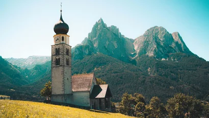 Kirche auf sonnigem Hügel mit Bergkette im Hintergrund
