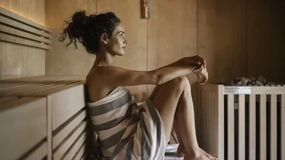 Woman wrapped in towel sitting relaxed in wooden sauna