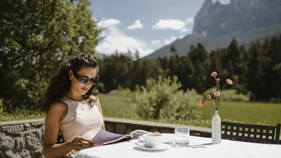 Woman reading magazine at outdoor table with mountain view