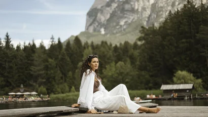 Woman sitting relaxed on a dock with forest and mountain background