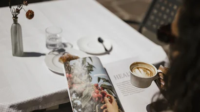 Person reading magazine holding coffee cup at table with white tablecloth