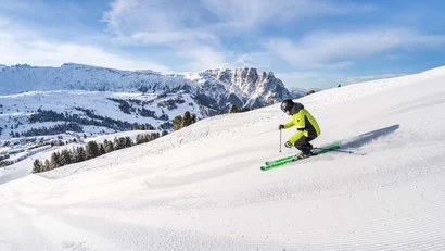 Skifahrer in grüner Jacke fährt auf schneebedecktem Hang bei Bergen