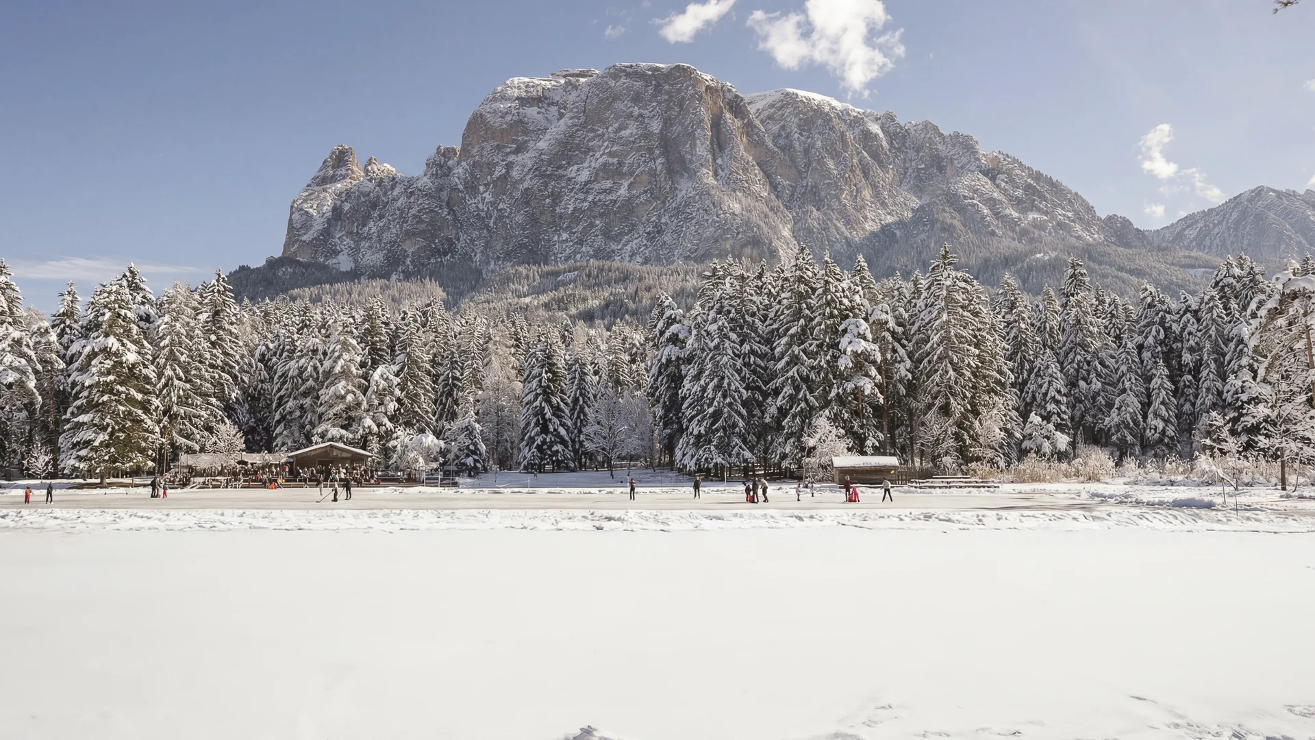 Schneebedeckte Bäume und Berge mit Menschen auf zugefrorenem See