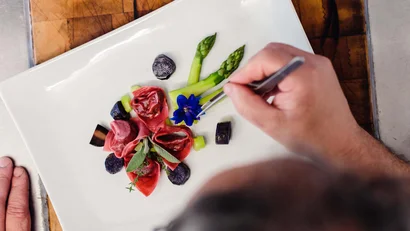 Hand richtet mit Pinzette blau blühende essbare Blume auf Teller mit Spargel
