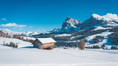 Verschneite Hütte vor Bergkulisse mit blauem Himmel