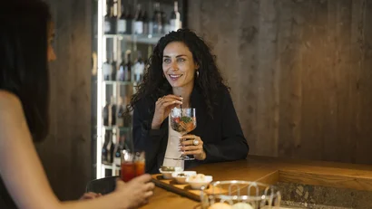 Two women chatting at a bar holding drinks