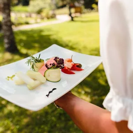 Person trägt Teller mit Gourmet-Gemüse und Lachs im Freien
