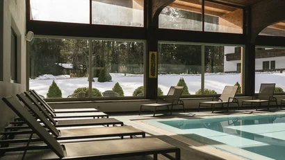Ruheliegen neben einem Innenpool mit Blick auf verschneite Landschaft durch große Fenster