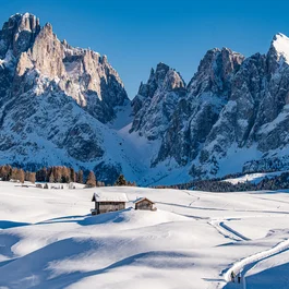 Schneebedeckte Alpenlandschaft mit Hütten und Bergen unter klarem blauem Himmel