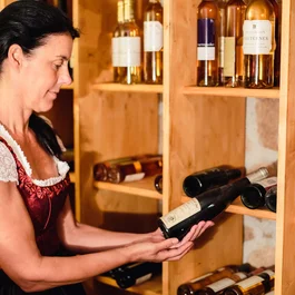 Frau im Dirndl hält Weinflasche in Weinkeller mit Holzregalen