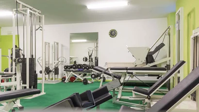 Fitnessstudio mit Trainingsgeräten und Hanteln vor weißer Wand