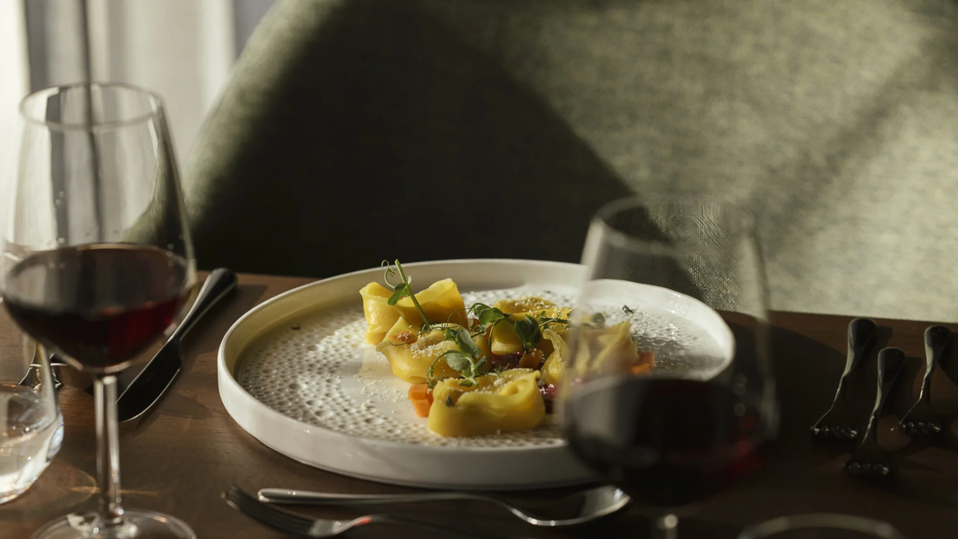 Teller mit Pasta und Gläser Rotwein auf einem gedeckten Tisch