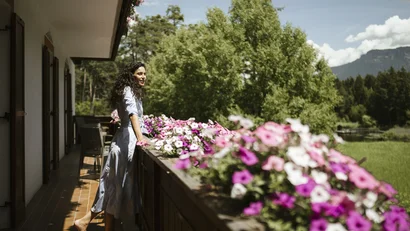 Barefoot woman on balcony with flowers overlooking green landscape