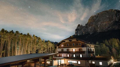 Beleuchtetes Hotel bei Nacht vor bewaldetem Berg und Sternenhimmel