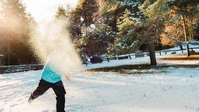 Person wirft Schnee in einem verschneiten Wald bei Sonnenlicht