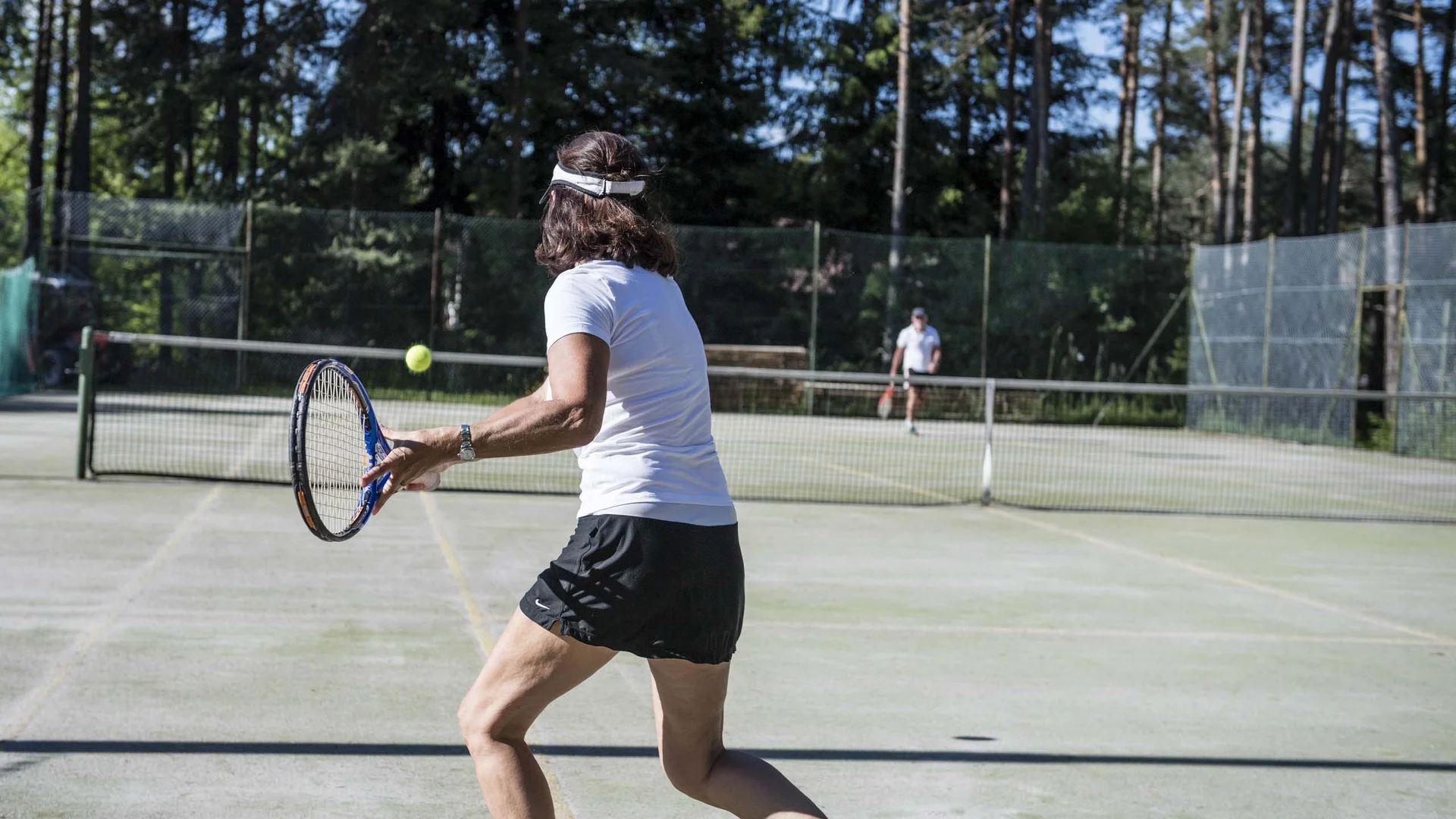 Frau spielt Tennis auf Außenplatz mit Wald im Hintergrund