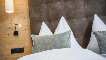 Gemütliches Bett mit floralen Kissen und braunem gepolstertem Kopfteil