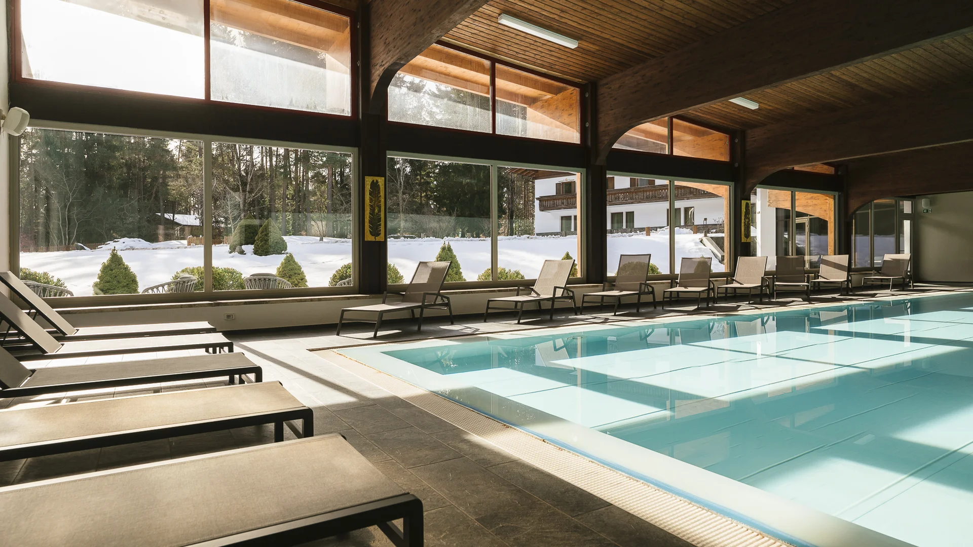 Innenpool mit Liegestühlen und Blick auf schneebedeckten Garten